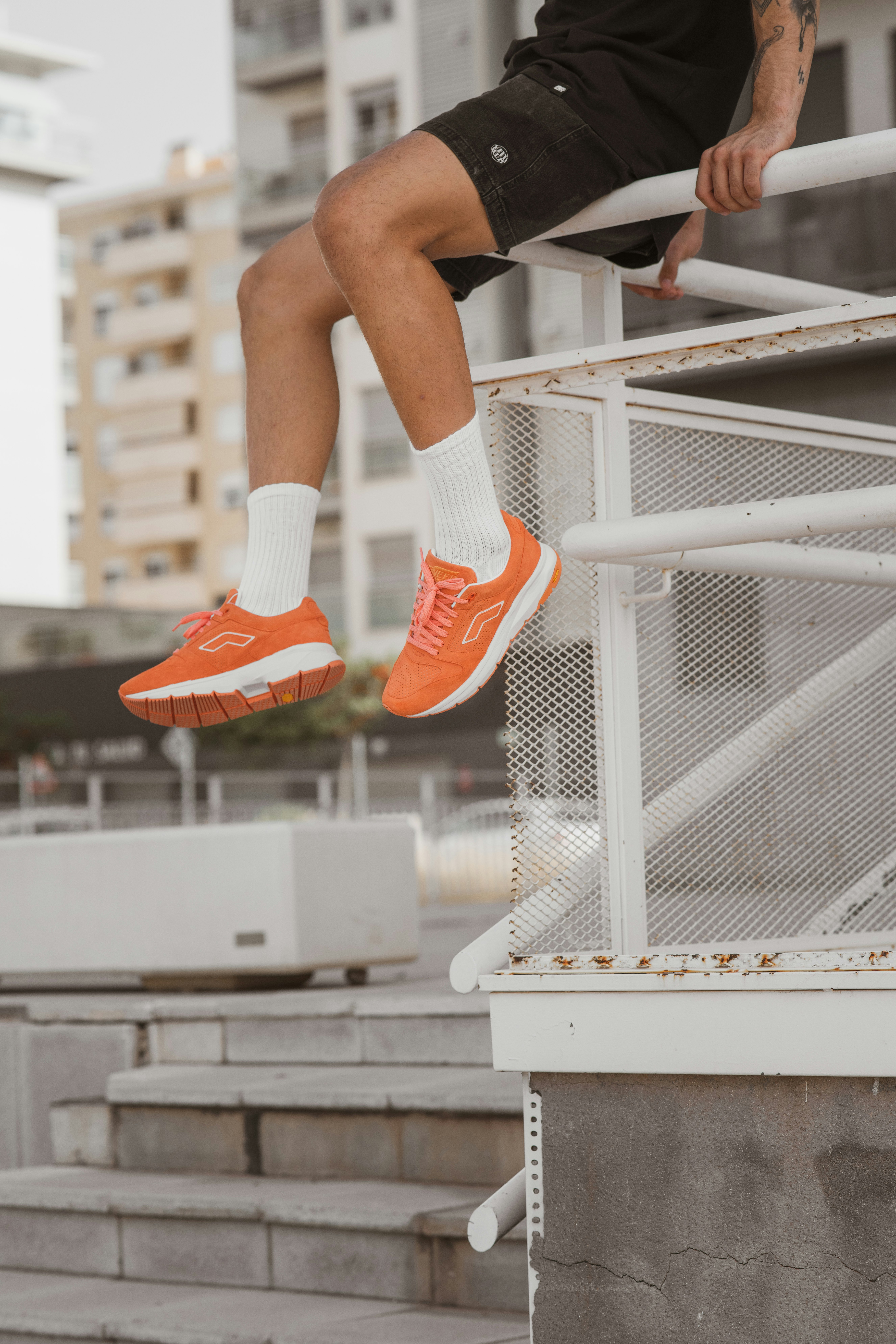 person in orange and white nike sneakers sitting on white metal railings
